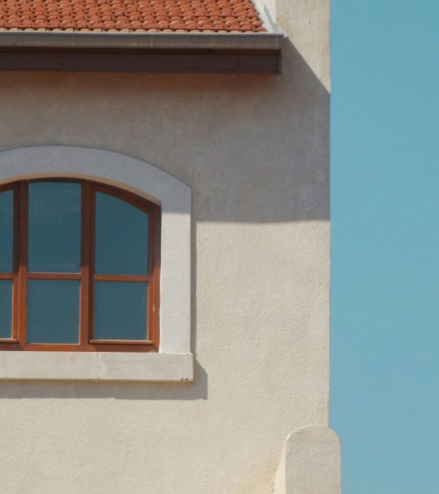 A close-up of a Mediterranean style building facade with red roof tiles and arched window.